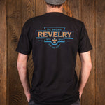 A man viewed from behind wearing a black t-shirt with a large graphic on the back. The graphic features the words 'THE ORIGINAL REVELRY SUPPLY COMPANY' and 'OFF THE CLOCK' in orange and blue.
